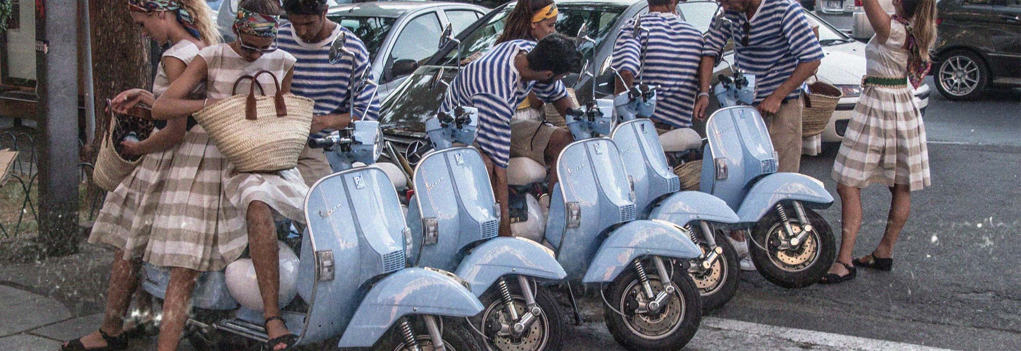 Junge italienische Männer und Frauen in gestreiften Hemden und Kleidern auf hellblauen Vespas